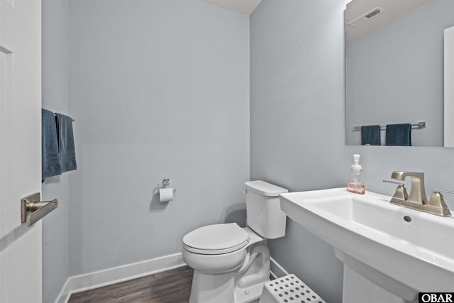 half bath featuring toilet, wood finished floors, a sink, visible vents, and baseboards