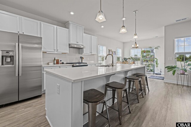 kitchen featuring under cabinet range hood, a sink, light countertops, range, and stainless steel fridge