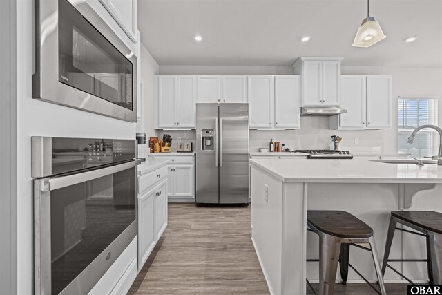 kitchen with a breakfast bar area, appliances with stainless steel finishes, light countertops, under cabinet range hood, and a sink