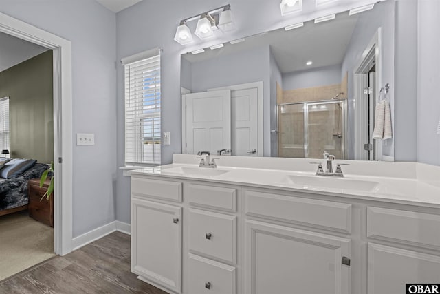 ensuite bathroom featuring a stall shower, a sink, baseboards, and wood finished floors