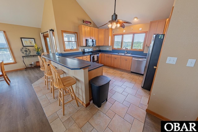 kitchen with stainless steel appliances, dark countertops, a kitchen bar, a sink, and a peninsula