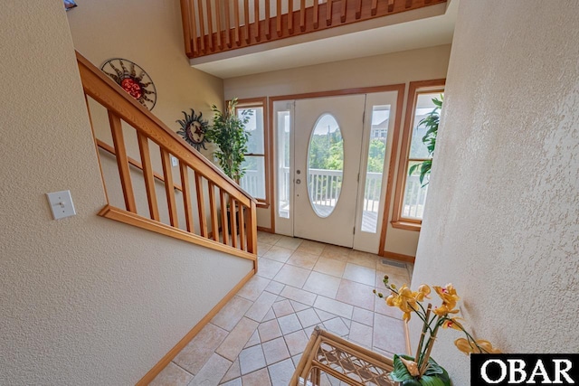 foyer featuring light tile patterned floors, stairs, a textured wall, and baseboards