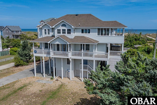 rear view of house featuring driveway, roof with shingles, and a water view