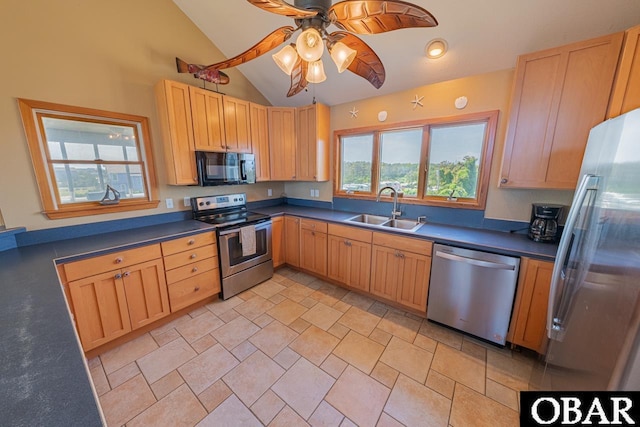 kitchen featuring light brown cabinetry, stainless steel appliances, dark countertops, a sink, and lofted ceiling