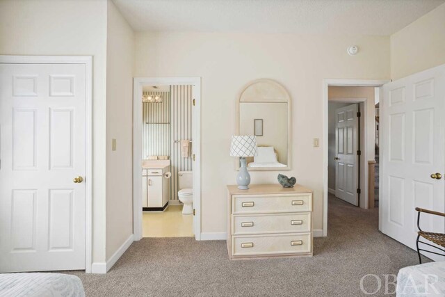 bedroom featuring light colored carpet, ensuite bath, and baseboards