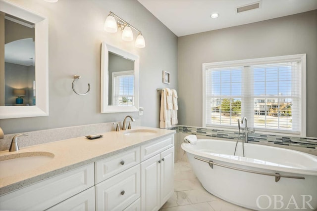 full bath featuring a freestanding tub, visible vents, a sink, and double vanity