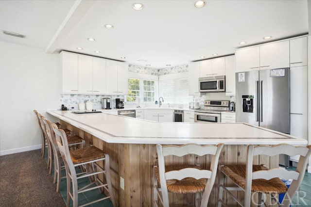 kitchen with stainless steel appliances, a breakfast bar, a sink, white cabinets, and light countertops