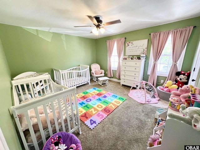carpeted bedroom with ceiling fan and a nursery area