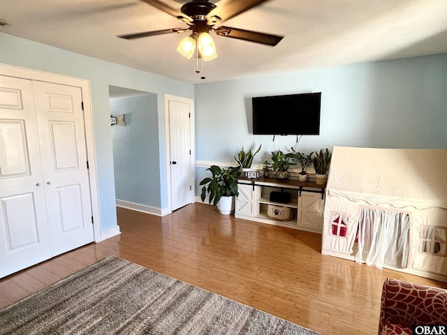 living area with baseboards, ceiling fan, and wood finished floors