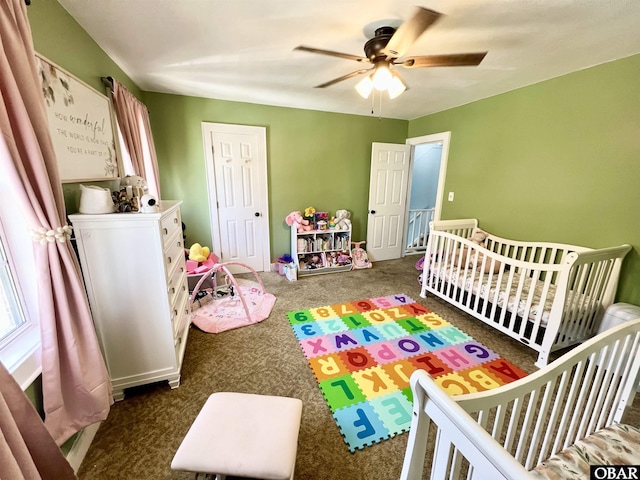 bedroom with a nursery area, a ceiling fan, and dark carpet
