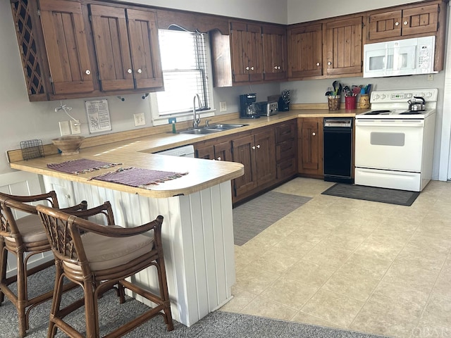 kitchen featuring white appliances, a kitchen bar, light countertops, and a sink