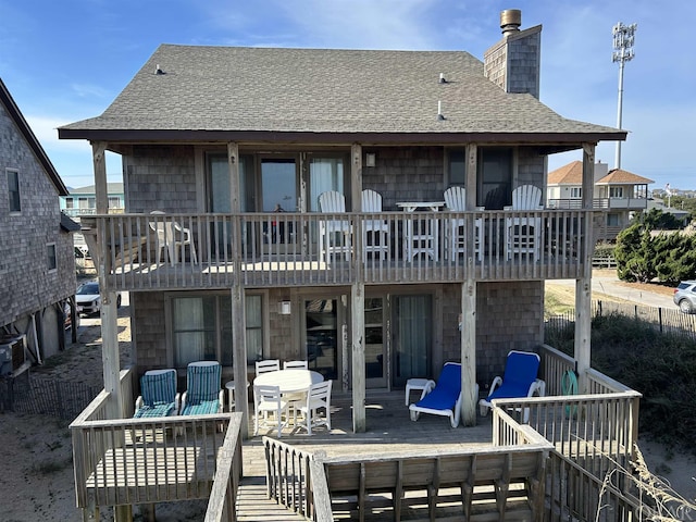 back of property with a deck, french doors, roof with shingles, and a chimney