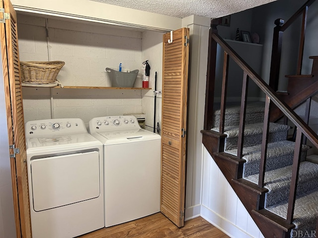 washroom with a textured ceiling, laundry area, separate washer and dryer, wood finished floors, and concrete block wall