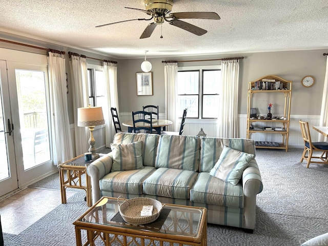 living area featuring a wainscoted wall, a textured ceiling, carpet, and a ceiling fan