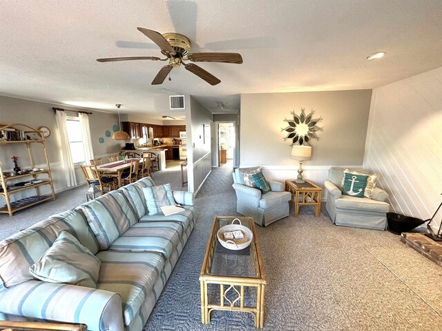 living room featuring a textured ceiling, carpet floors, ceiling fan, and visible vents