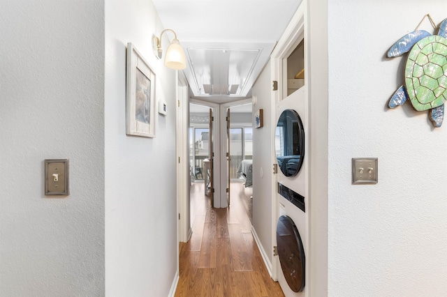 hallway featuring stacked washing maching and dryer, attic access, baseboards, and wood finished floors