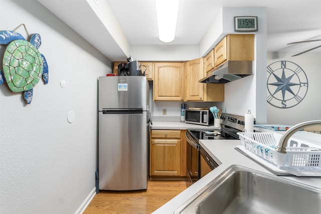 kitchen featuring appliances with stainless steel finishes, light countertops, light wood-type flooring, under cabinet range hood, and a sink