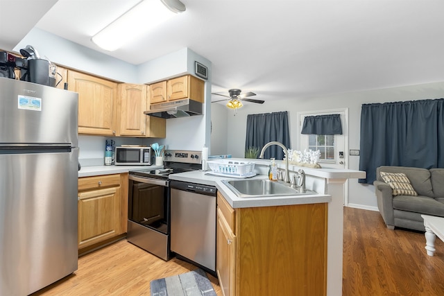 kitchen featuring under cabinet range hood, stainless steel appliances, a sink, light wood-style floors, and light countertops