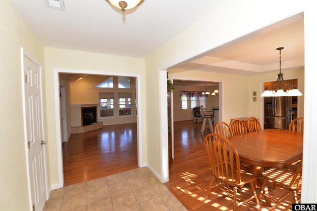 dining space featuring a notable chandelier, light tile patterned floors, visible vents, a fireplace with raised hearth, and baseboards