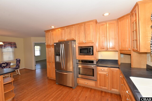 kitchen featuring recessed lighting, stainless steel appliances, a sink, light wood finished floors, and dark countertops