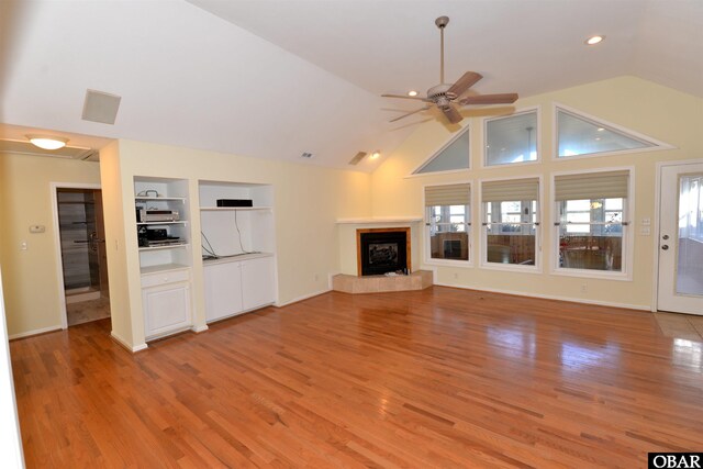 unfurnished living room with built in shelves, a tile fireplace, lofted ceiling, and light wood finished floors