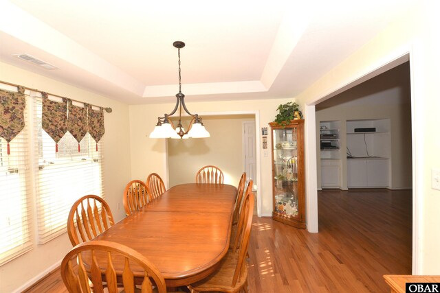 dining space featuring baseboards, visible vents, a tray ceiling, light wood-type flooring, and a notable chandelier