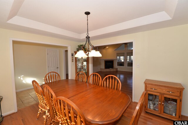 dining room featuring light wood-type flooring, baseboards, a tray ceiling, and a notable chandelier