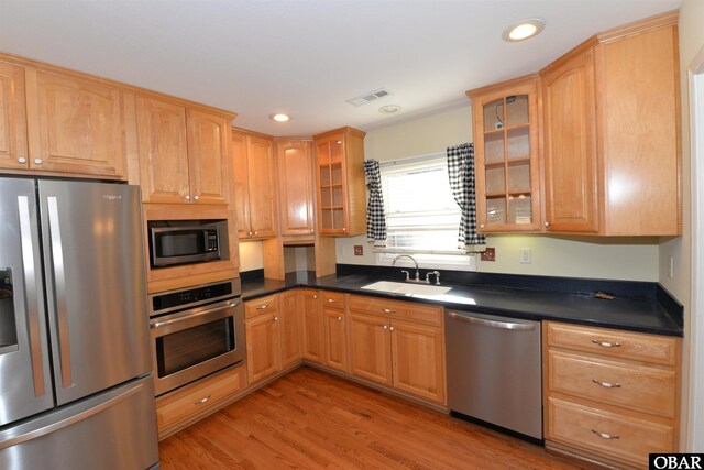 kitchen featuring light wood-type flooring, appliances with stainless steel finishes, dark countertops, and a sink