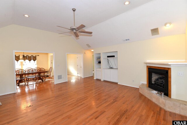 living area featuring lofted ceiling, a fireplace with raised hearth, visible vents, and light wood finished floors