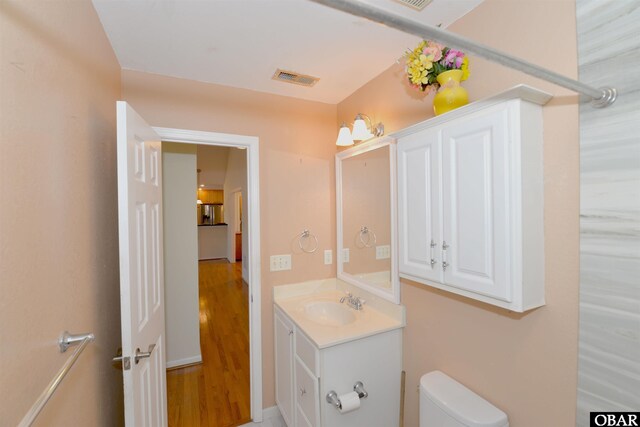 half bathroom with toilet, visible vents, wood finished floors, and vanity