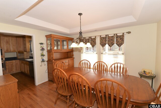 dining space featuring a chandelier, a raised ceiling, baseboards, and wood finished floors