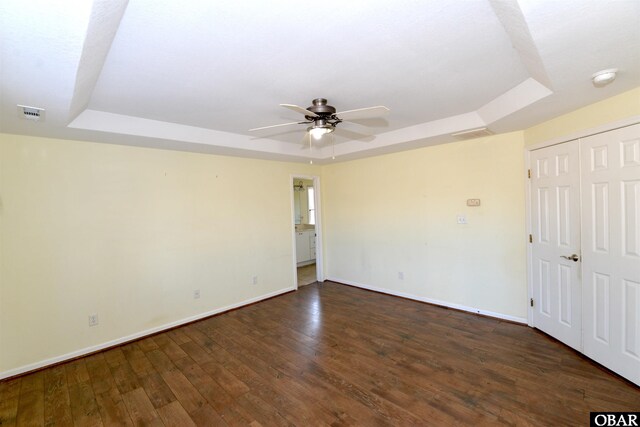 interior space with a tray ceiling, wood-type flooring, and baseboards