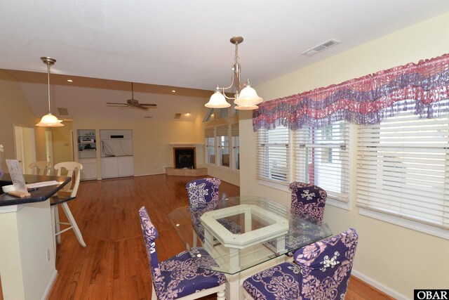 dining room featuring vaulted ceiling, visible vents, a fireplace with raised hearth, and wood finished floors