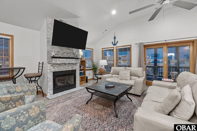 living room featuring a ceiling fan, high vaulted ceiling, wood finished floors, and a stone fireplace