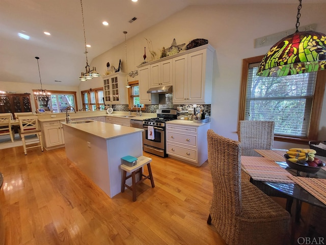 kitchen featuring glass insert cabinets, stainless steel range with gas cooktop, light countertops, and hanging light fixtures