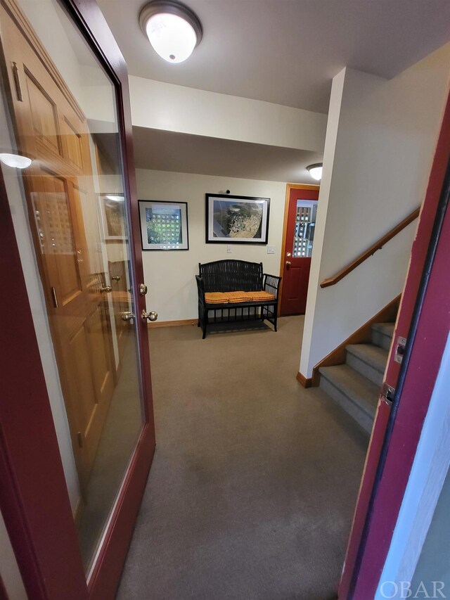 corridor featuring dark carpet, stairway, and baseboards