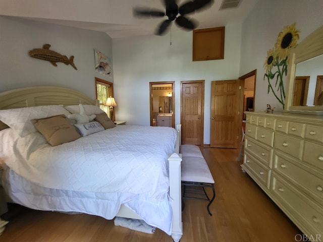 bedroom featuring light wood-style floors, visible vents, high vaulted ceiling, and ensuite bath