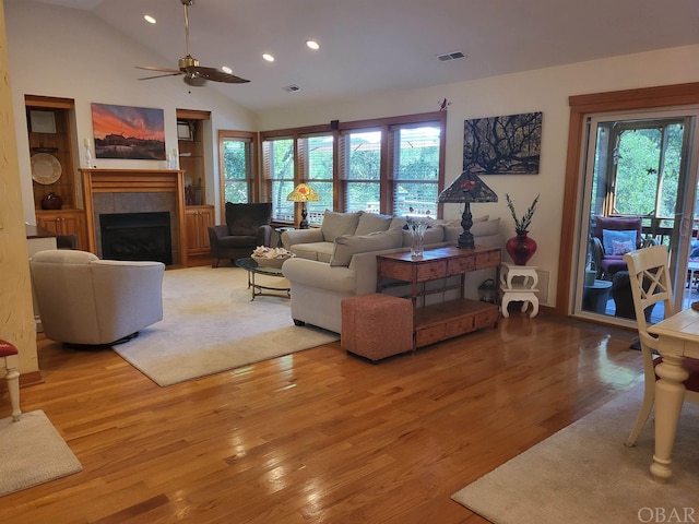 living room with light wood finished floors, recessed lighting, visible vents, a tiled fireplace, and vaulted ceiling