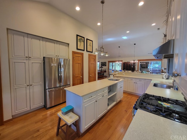 kitchen featuring appliances with stainless steel finishes, decorative light fixtures, a kitchen island with sink, light countertops, and under cabinet range hood