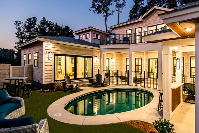 back of property at dusk with a patio, fence, a balcony, and a fenced in pool