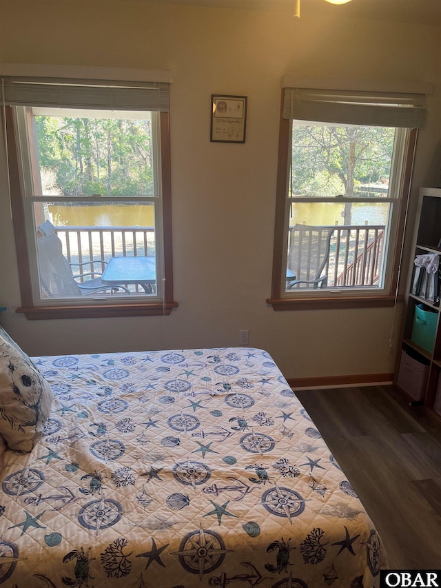 bedroom with a water view, multiple windows, baseboards, and wood finished floors