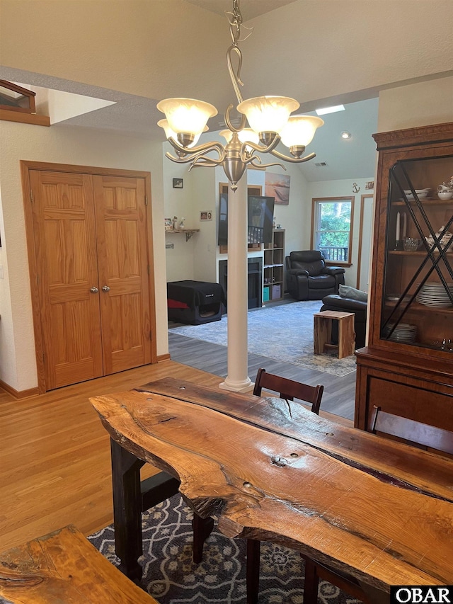 dining space featuring lofted ceiling, a notable chandelier, light wood-style flooring, and decorative columns