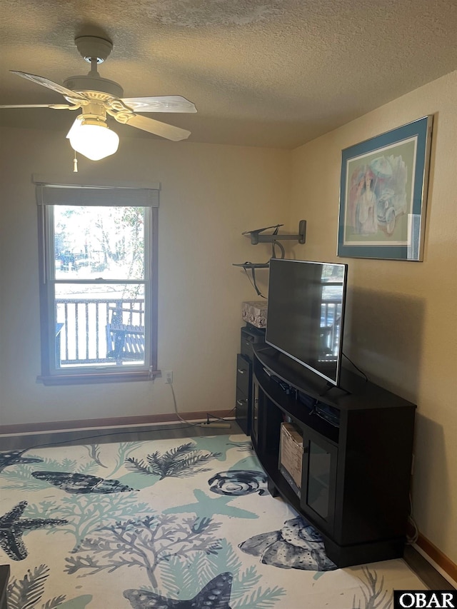 living room featuring a textured ceiling, ceiling fan, and baseboards