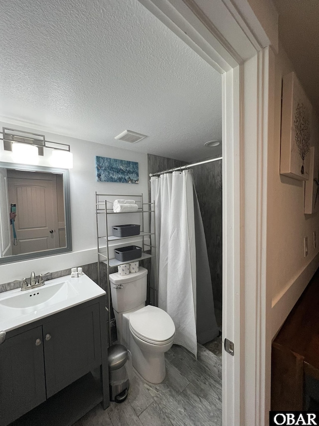 full bath with a textured ceiling, curtained shower, toilet, vanity, and visible vents