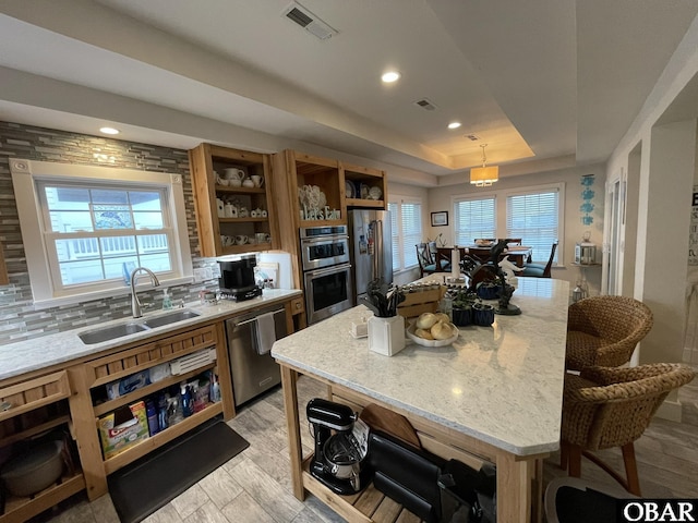 kitchen featuring light stone counters, stainless steel appliances, a sink, open shelves, and a raised ceiling