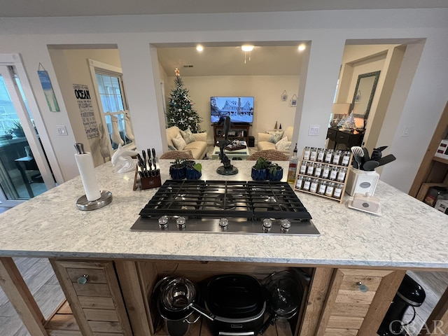 kitchen with stainless steel gas cooktop, open floor plan, light stone counters, and a center island