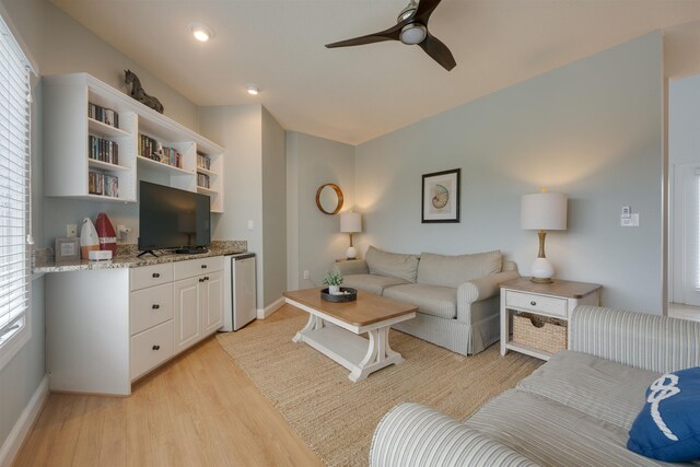 living area featuring baseboards, light wood-style flooring, and a ceiling fan