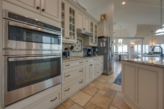 kitchen featuring stone tile floors, appliances with stainless steel finishes, decorative light fixtures, cream cabinets, and under cabinet range hood