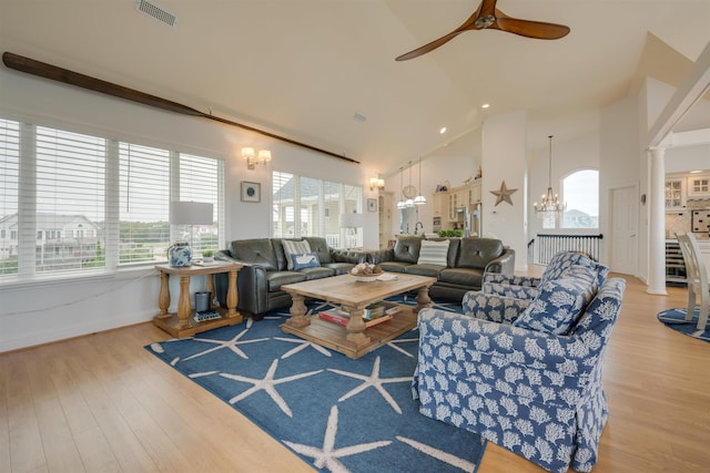 living area with light wood-style floors, visible vents, high vaulted ceiling, and ornate columns