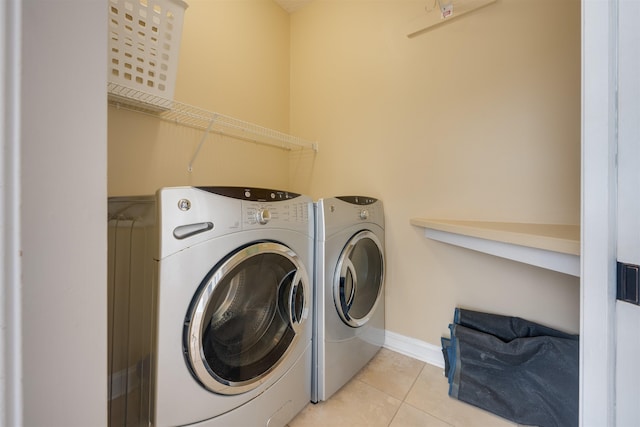 laundry room with light tile patterned floors, laundry area, washing machine and dryer, and baseboards